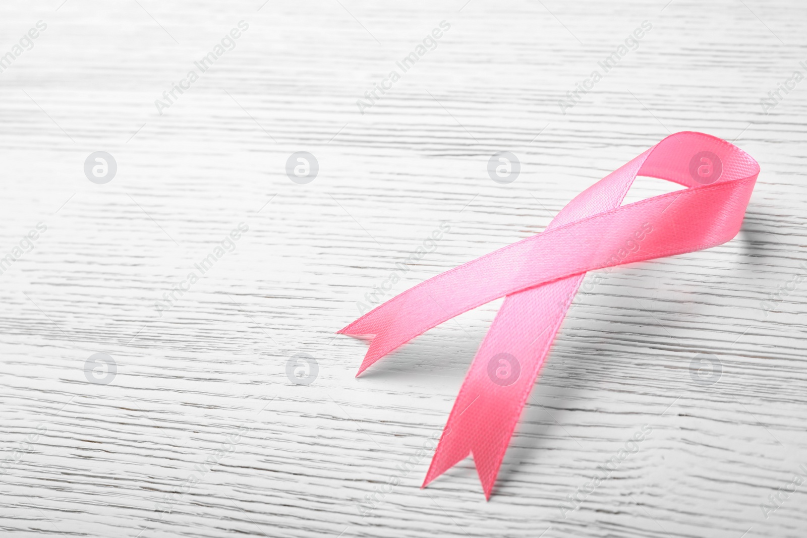 Photo of Pink ribbon on wooden background, space for text. Breast cancer awareness concept
