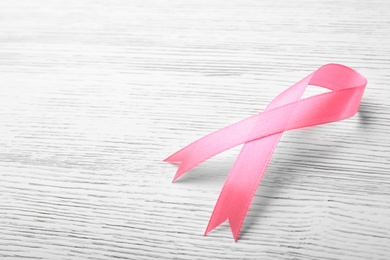 Photo of Pink ribbon on wooden background, space for text. Breast cancer awareness concept