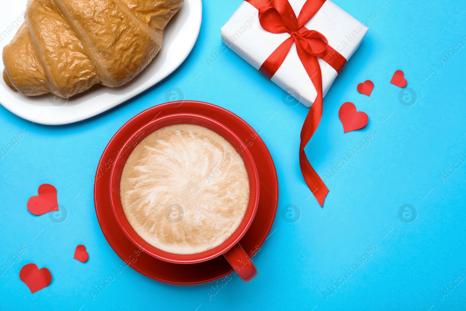 Photo of Cup of coffee, croissant and gift box on turquoise background, flat lay. Valentine's day breakfast