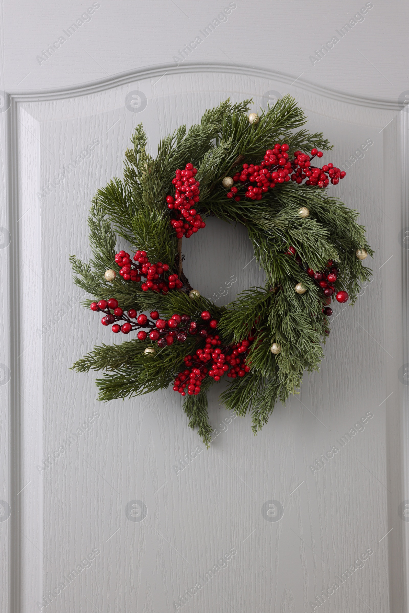Photo of Beautiful Christmas wreath with red berries and decor hanging on white door