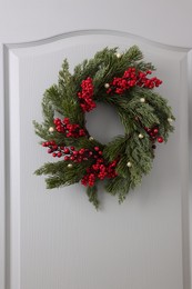 Beautiful Christmas wreath with red berries and decor hanging on white door