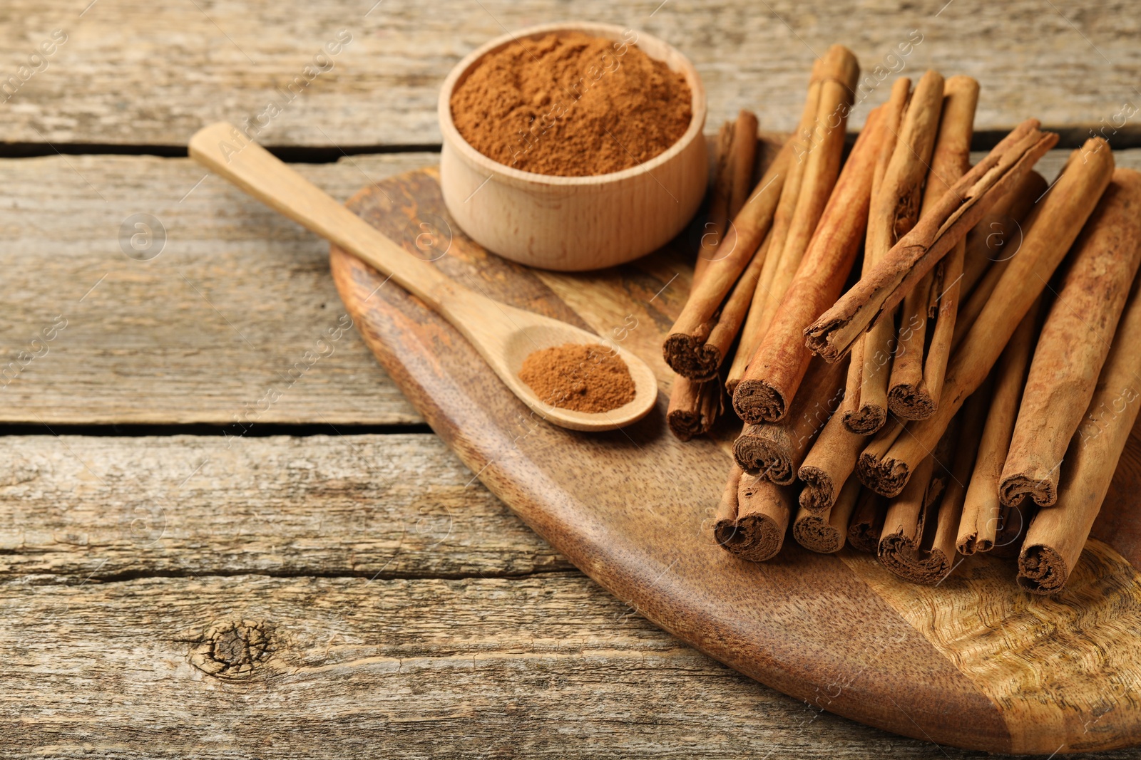 Photo of Cinnamon powder and sticks on wooden table. Space for text