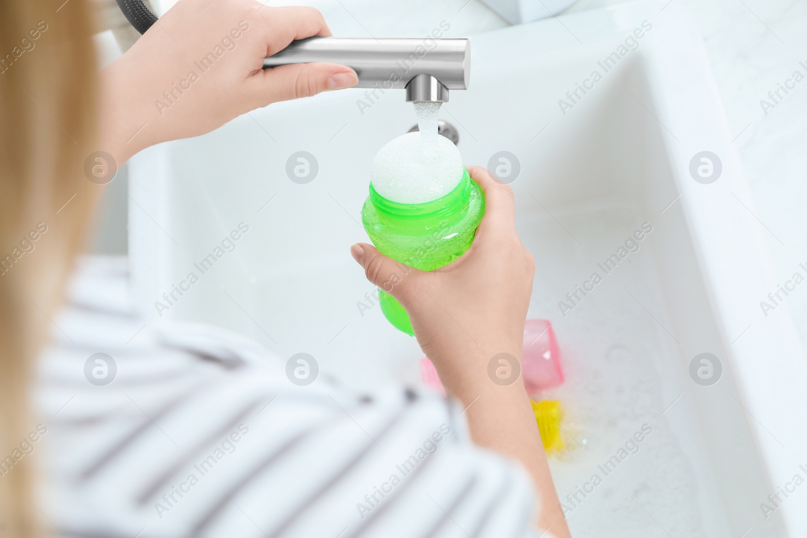 Photo of Woman washing baby bottle under stream of water in kitchen, above view