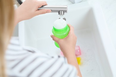 Woman washing baby bottle under stream of water in kitchen, above view