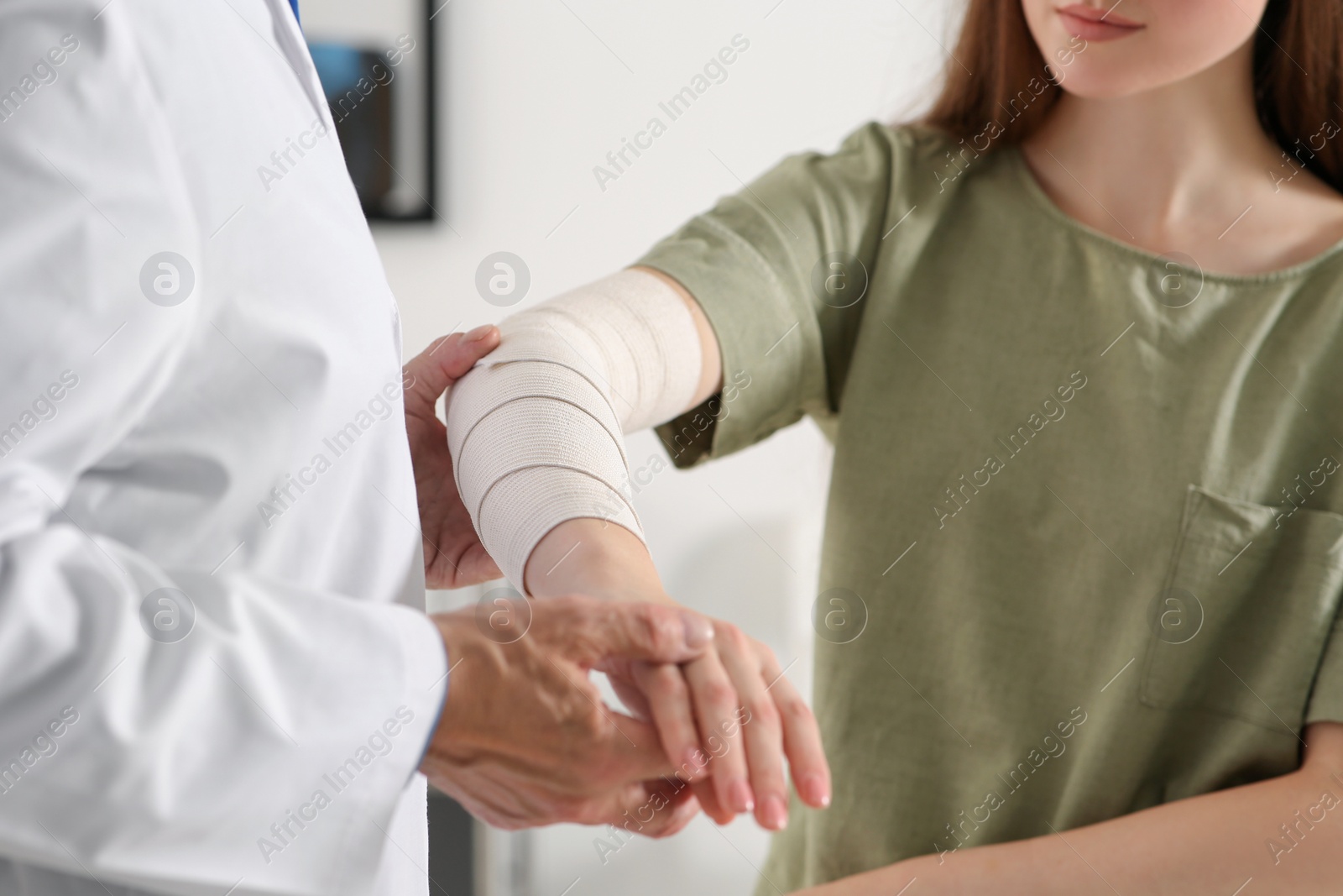 Photo of Orthopedist applying bandage onto patient's elbow in clinic, closeup