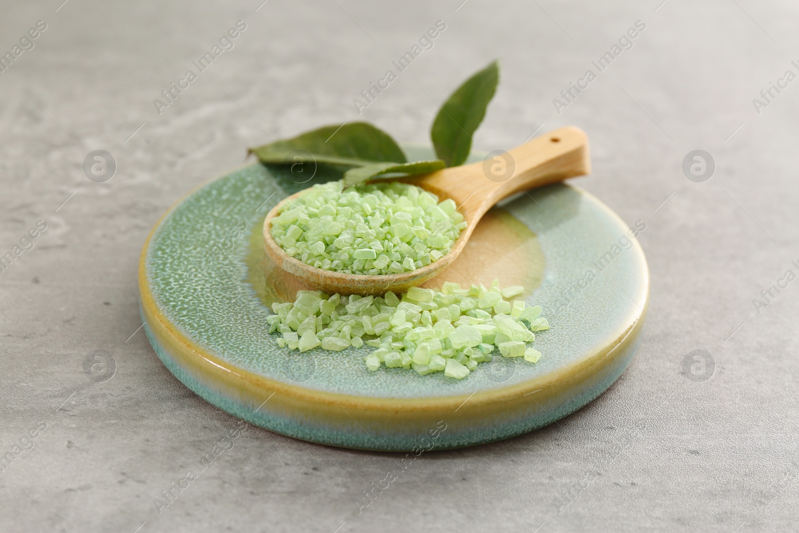 Photo of Aromatic sea salt and green leaves on grey textured table