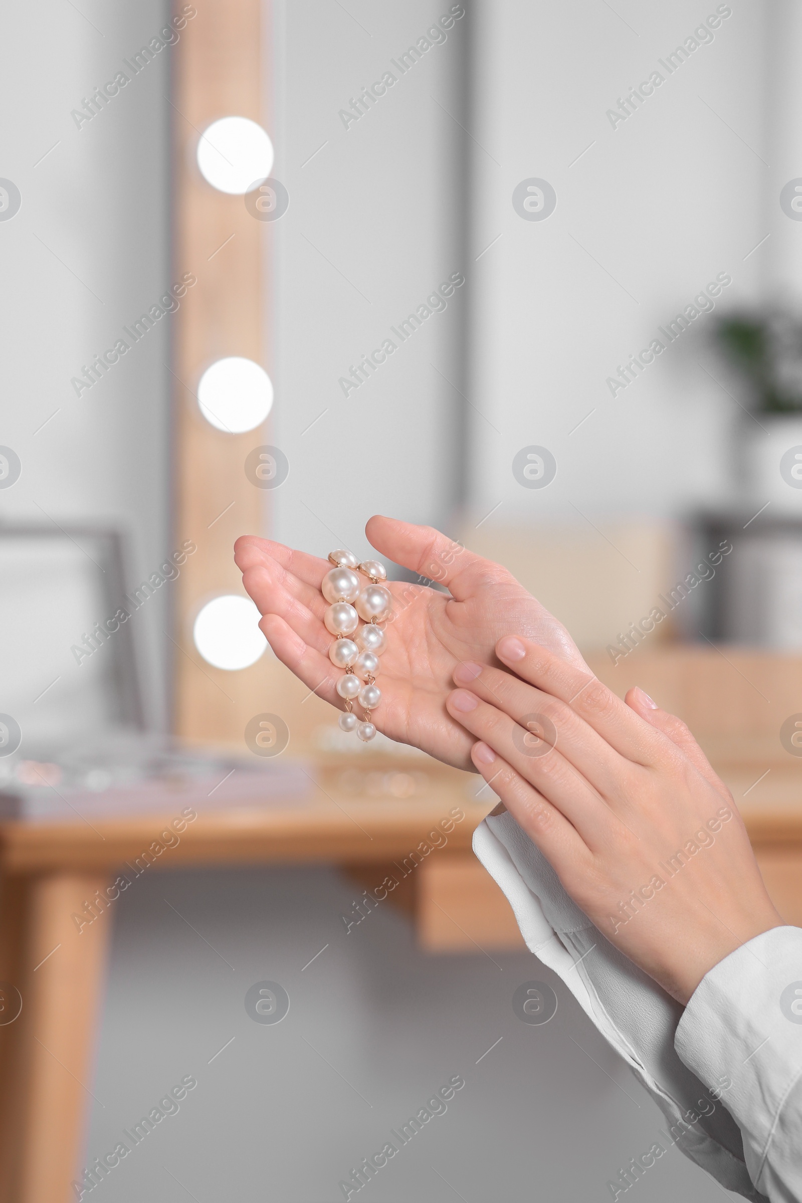 Photo of Young woman holding elegant pearl earings indoors, closeup