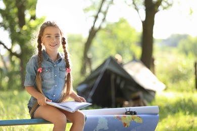Photo of Little girl with map and book near tent outdoors. Summer camp