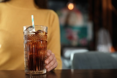 Woman with glass of refreshing cola at table indoors, closeup. Space for text