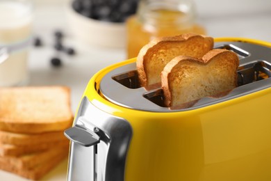 Photo of Modern yellow toaster with roasted bread slices on table, closeup