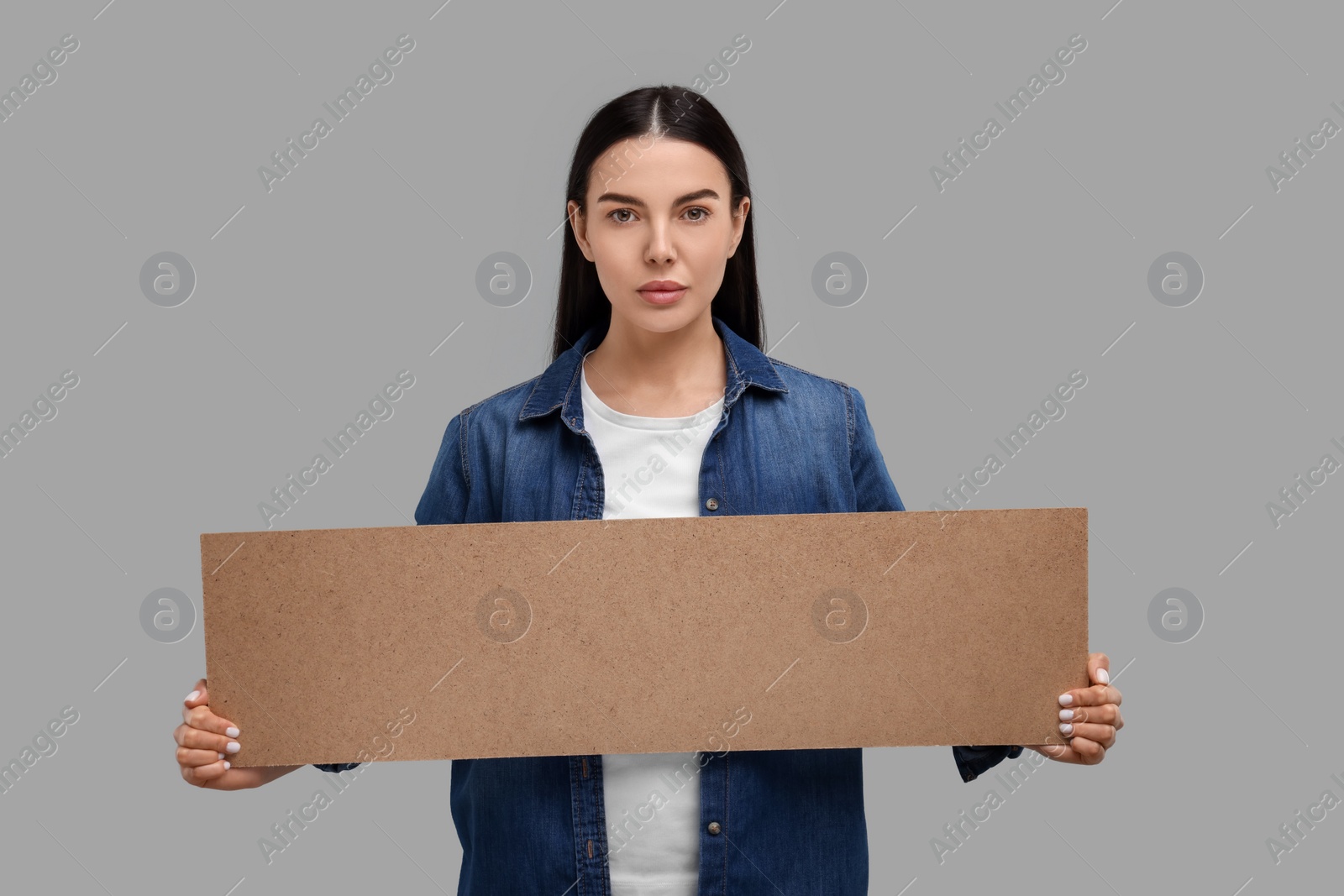 Photo of Woman holding blank cardboard banner on grey background, space for text