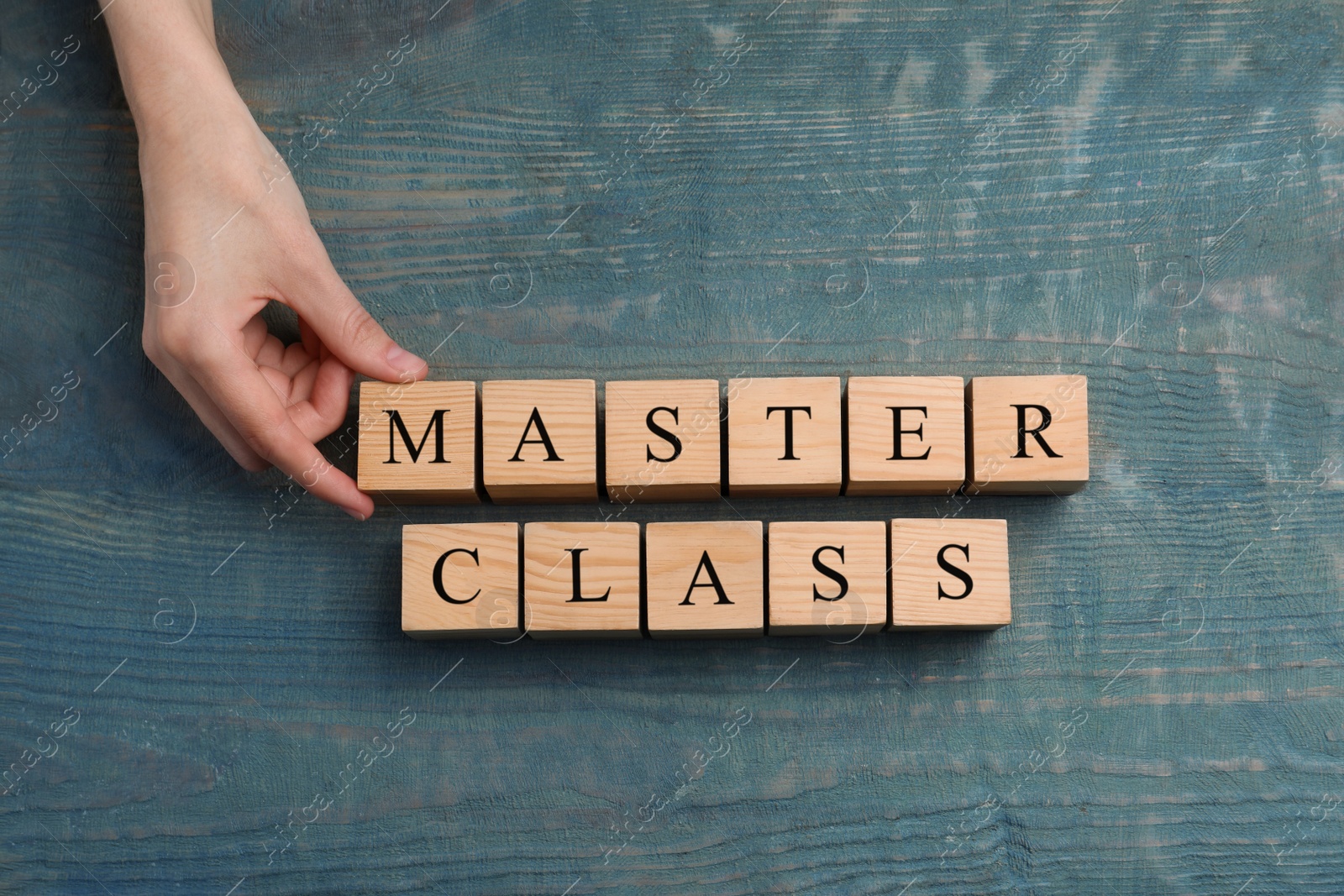 Photo of Woman making words Master Class with cubes at light blue wooden table, top view