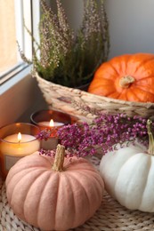 Photo of Wicker basket with beautiful heather flowers, pumpkins and burning candles near window indoors