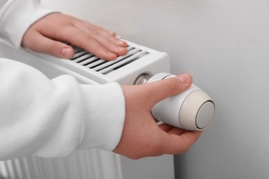Photo of Girl adjusting heating radiator thermostat near beige wall, closeup