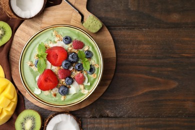 Photo of Tasty matcha smoothie bowl served with fresh fruits and oatmeal on wooden table, flat lay with space for text. Healthy breakfast