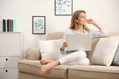 Photo of Pretty young woman with laptop sitting on sofa at home