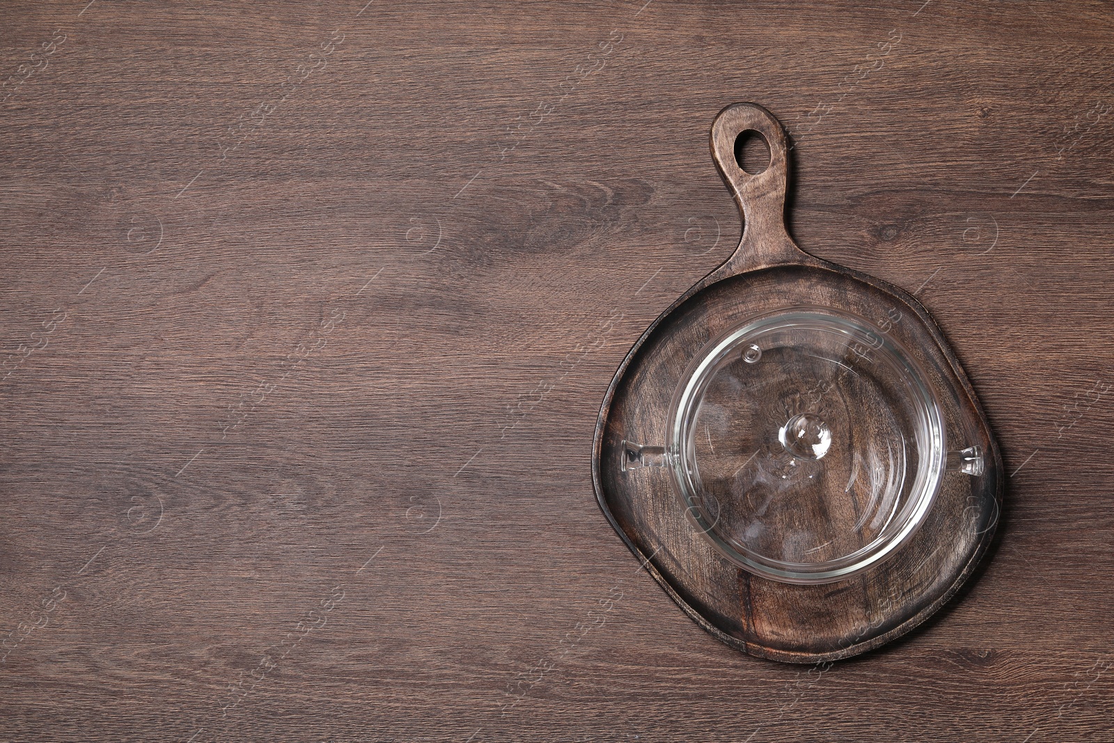 Photo of Empty glass pot and serving board on wooden table, top view. Space for text