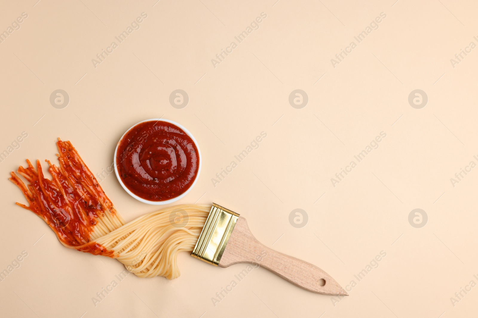 Photo of Brush painting with spaghetti dipped in ketchup on beige background, flat lay. Space for text. Creative concept