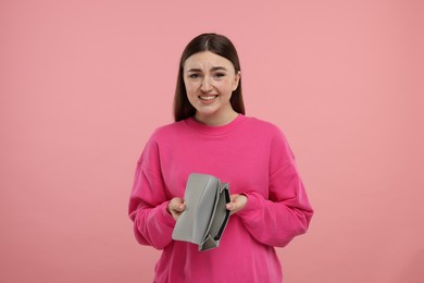 Woman showing empty wallet on pink background