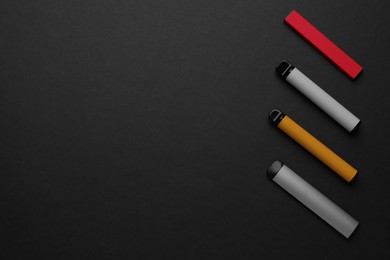 Photo of Disposable electronic smoking devices on black background, flat lay. Space for text