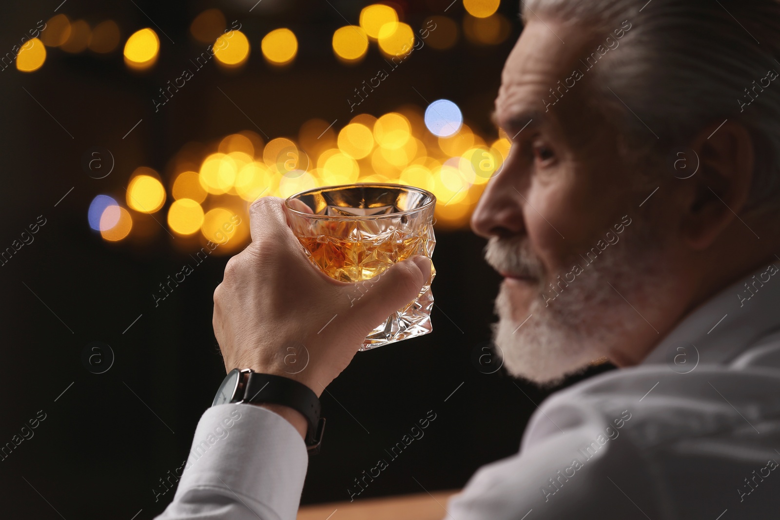 Photo of Senior man with glass of whiskey against blurred lights, closeup