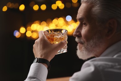 Photo of Senior man with glass of whiskey against blurred lights, closeup