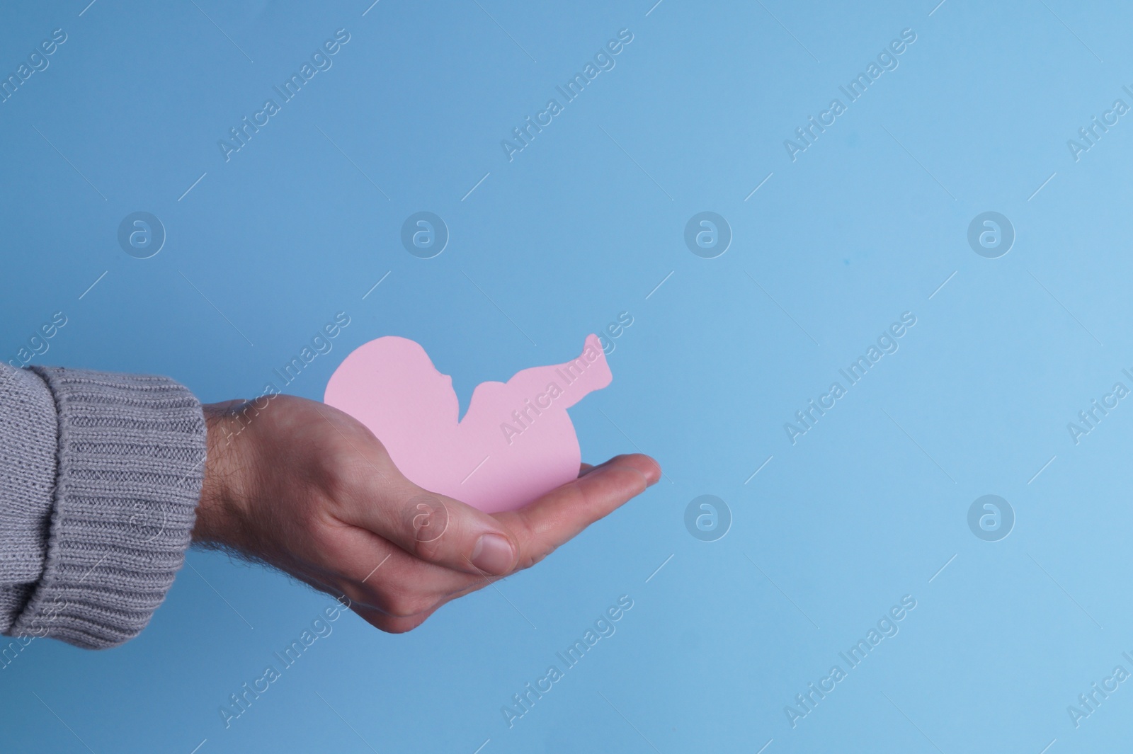 Photo of Female health. Man holding newborn paper figure on light blue background, closeup. Space for text