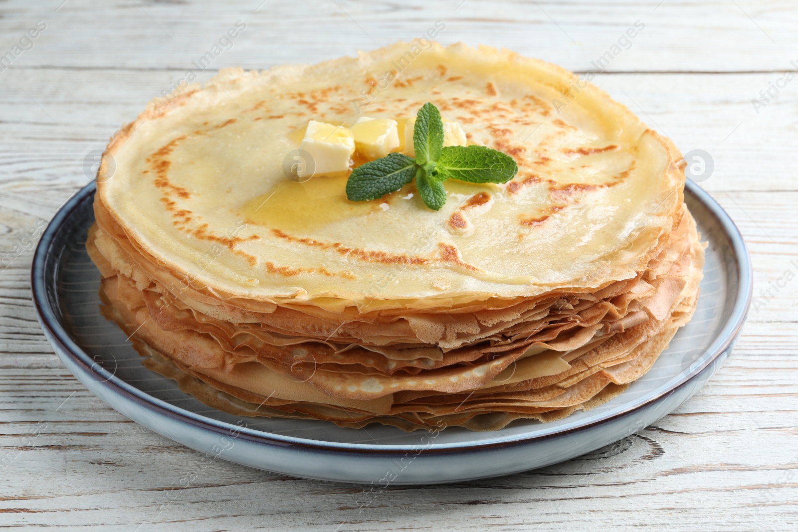 Photo of Stack of delicious crepes with mint and melting butter on white wooden table, closeup