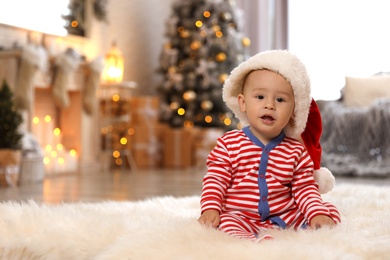 Photo of Little baby wearing Santa hat on floor at home. First Christmas