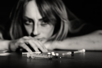 Photo of Addicted woman at table, focus on drugs. Black and white effect