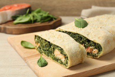 Photo of Delicious strudel with salmon and spinach served on light wooden table, closeup