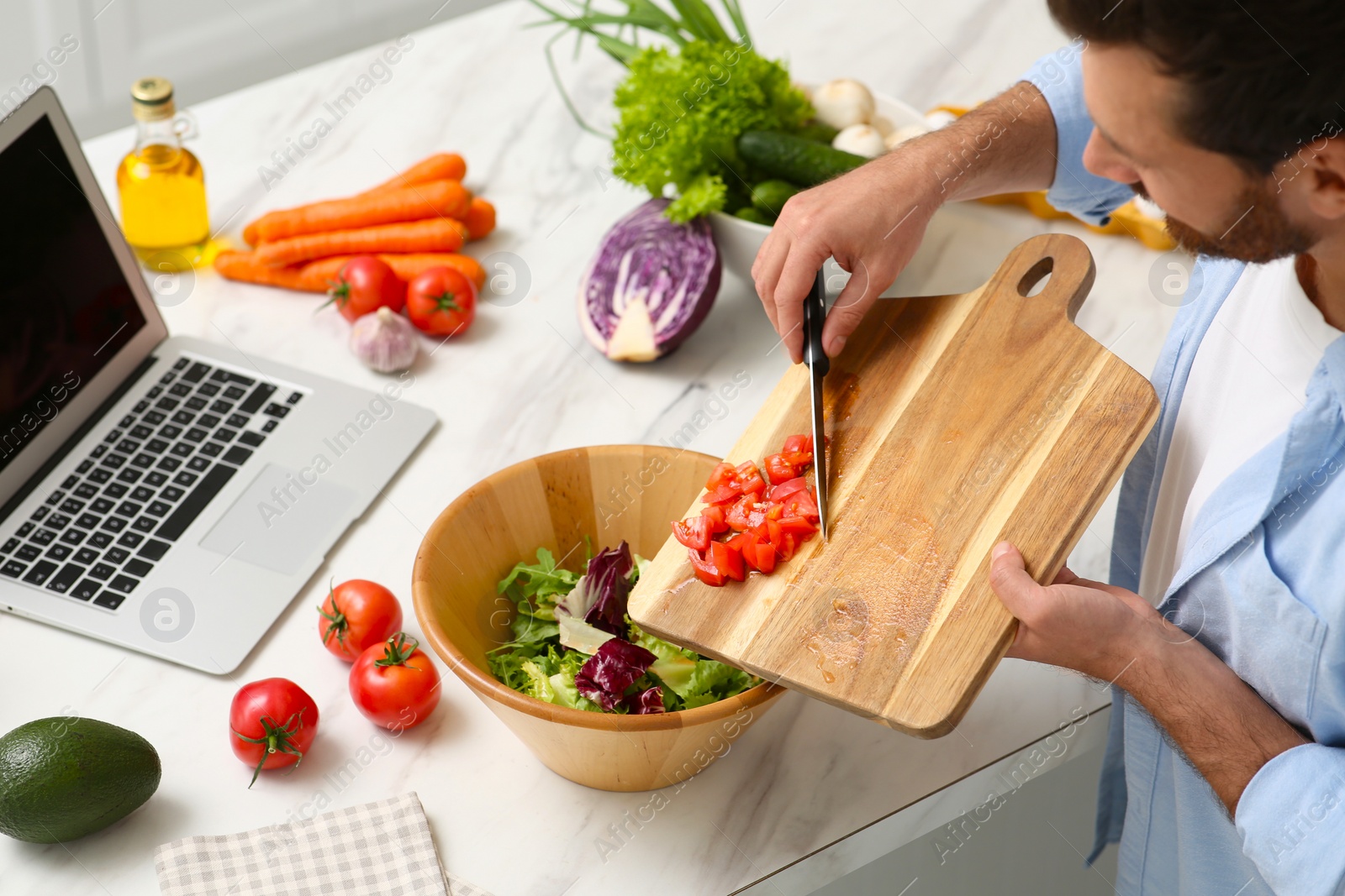 Photo of Man making dinner while watching online cooking course via laptop in kitchen, above view