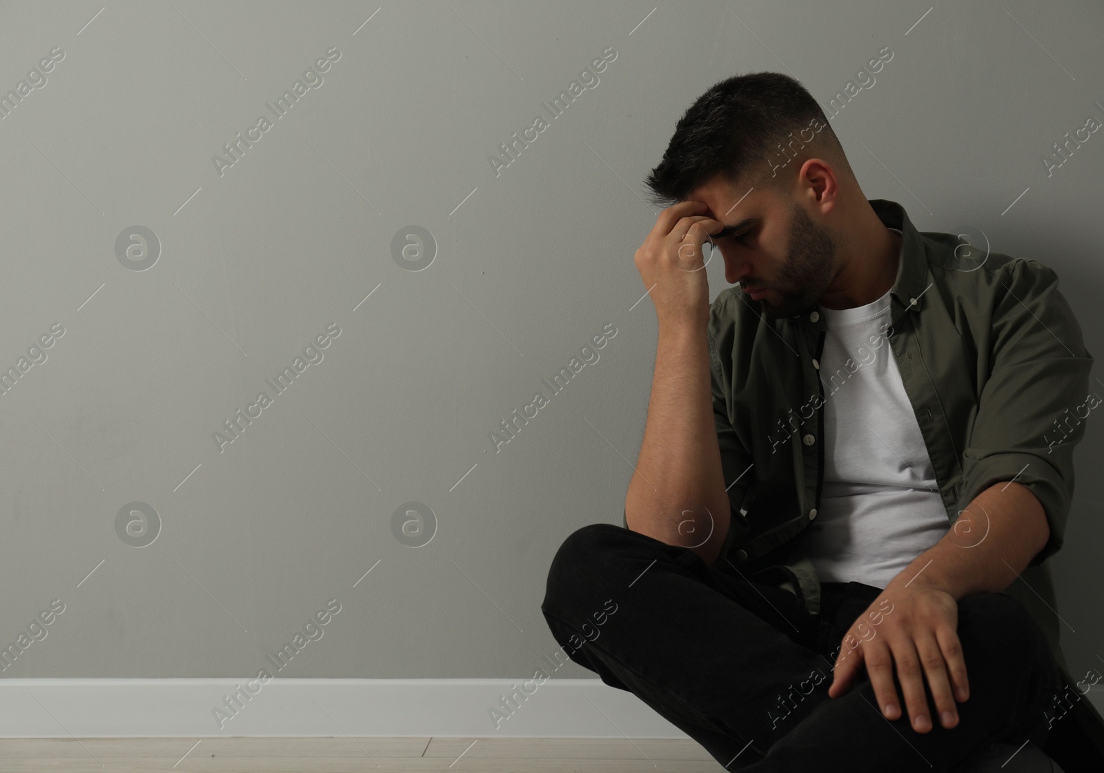 Photo of Sad man sitting on floor near light grey wall. Space for text