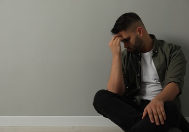 Photo of Sad man sitting on floor near light grey wall. Space for text