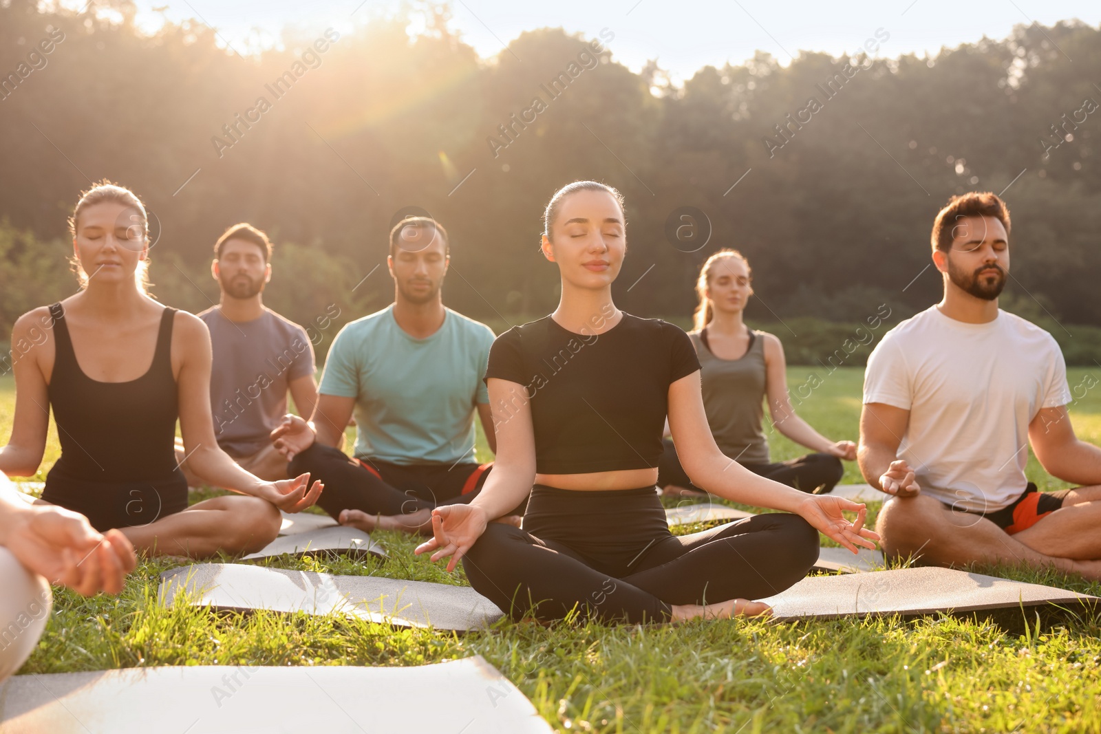 Photo of Group of people practicing yoga outdoors on sunny day, selective focus. Lotus pose