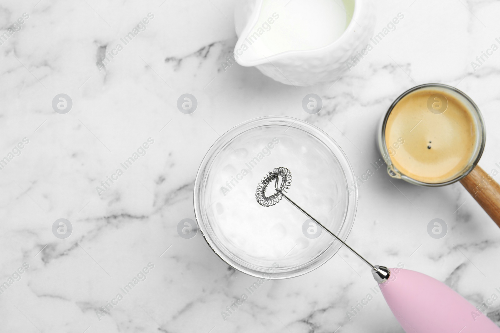 Photo of Flat lay composition with mini mixer (milk frother), whipped milk in glass and coffee at white marble table. Space for text