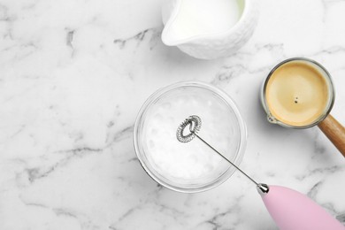 Photo of Flat lay composition with mini mixer (milk frother), whipped milk in glass and coffee at white marble table. Space for text