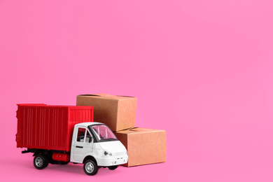 Photo of Truck model and carton boxes on pink background, space for text. Courier service