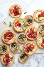 Different delicious canapes on white marble table, flat lay