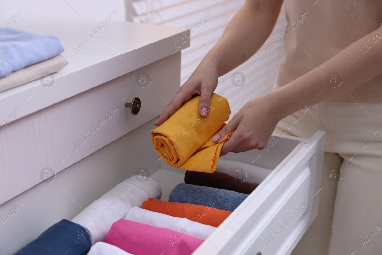 Photo of Woman putting rolled shirt into drawer at home, closeup. Organizing clothes