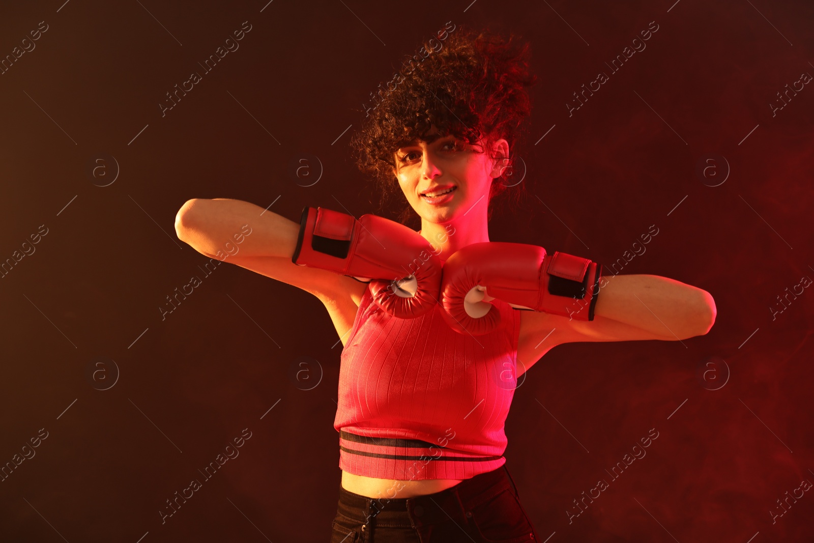 Photo of Beautiful young woman with boxing gloves on color background in neon lights and smoke