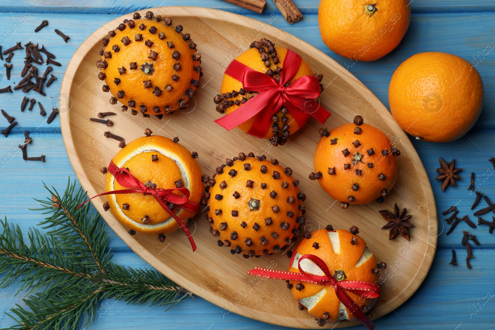 Photo of Pomander balls made of tangerines with cloves and fir branch on light blue wooden table, flat lay