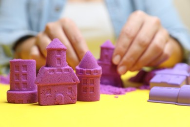 Photo of Woman playing with kinetic sand at yellow table, selective focus