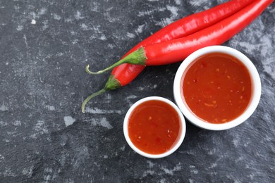 Photo of Spicy chili sauce and peppers on black textured table, flat lay. Space for text