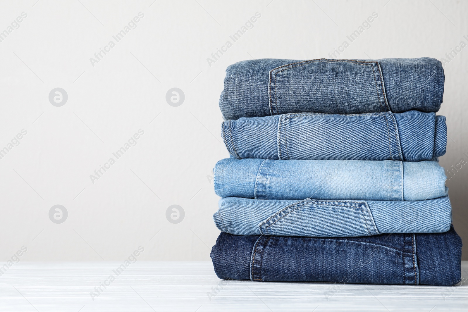 Photo of Stack of different jeans on white wooden table. Space for text