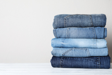 Photo of Stack of different jeans on white wooden table. Space for text