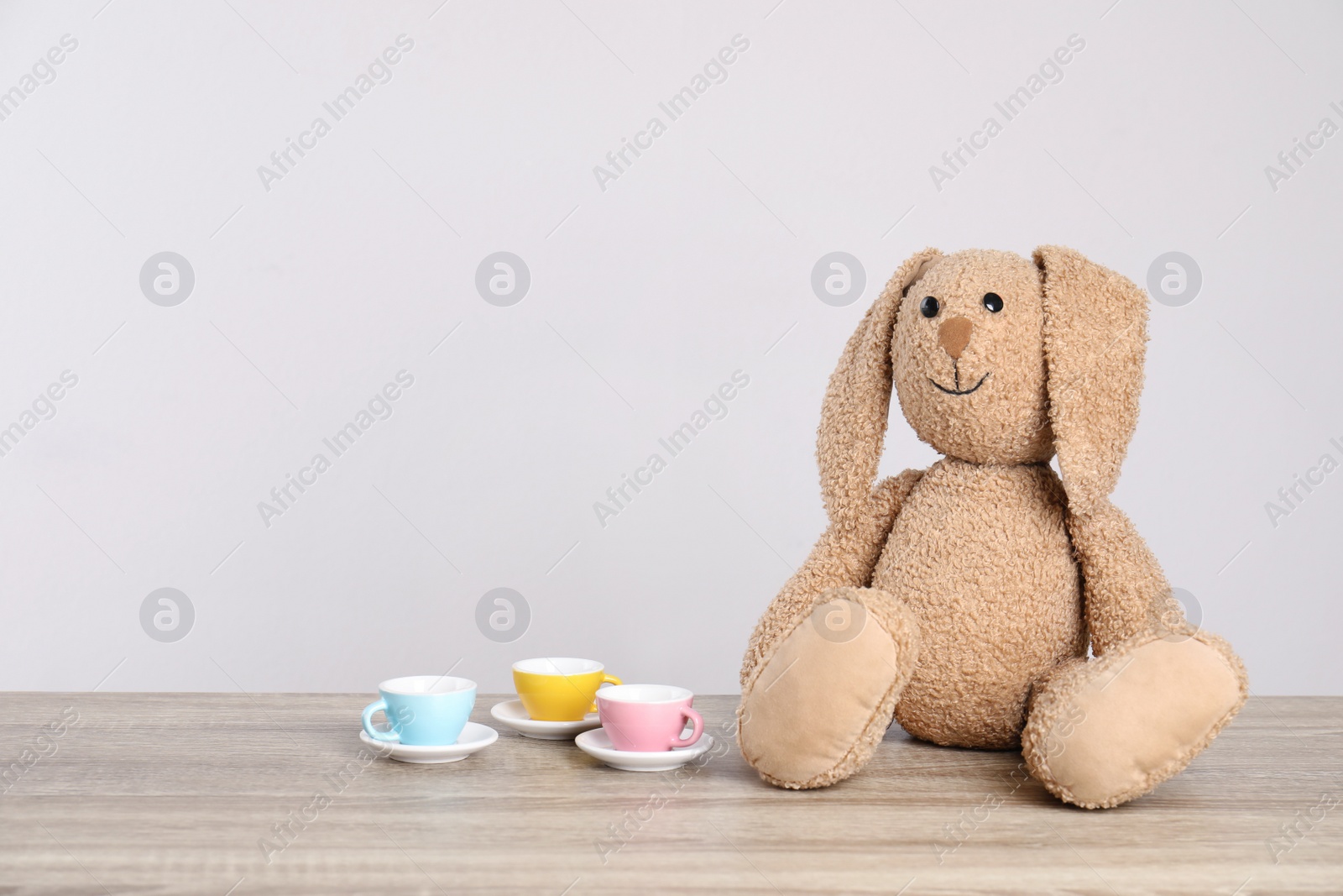 Photo of Adorable plush bunny and toy tableware on table against light background, space for text. Child room elements