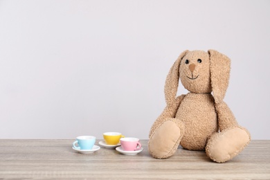 Adorable plush bunny and toy tableware on table against light background, space for text. Child room elements