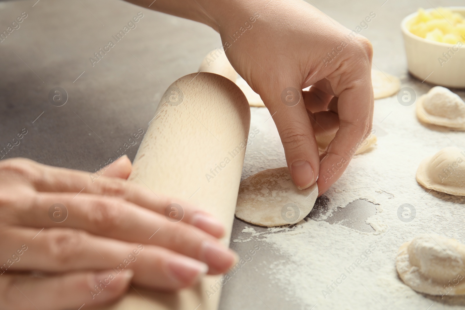 Photo of Woman with rolling pin cooking delicious dumplings at table, closeup