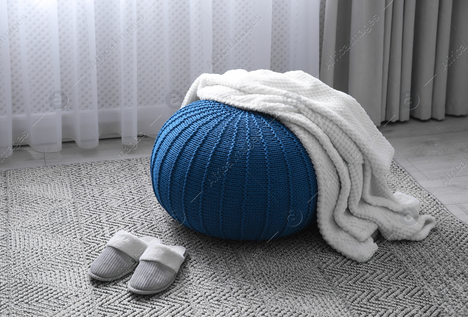 Photo of Soft blanket on blue pouf and slippers in room